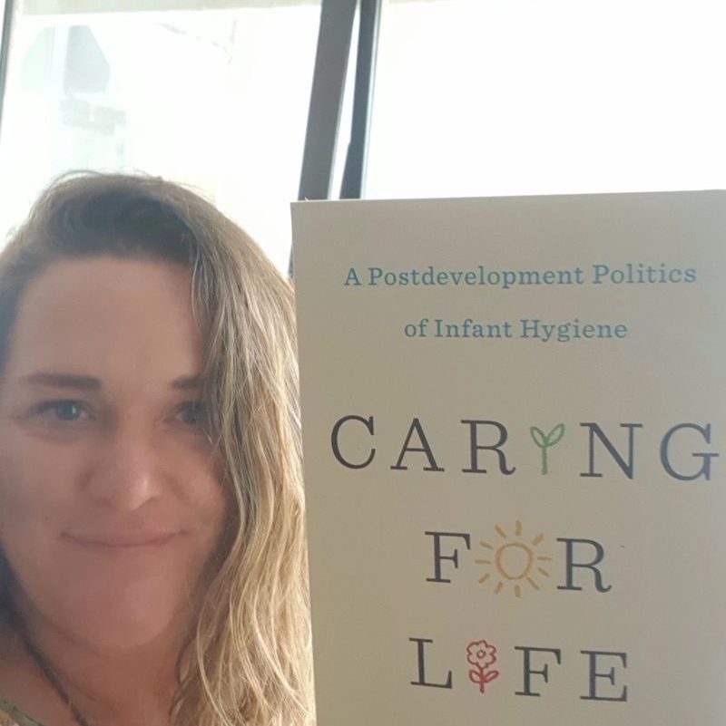 The author holds up a copy of the book Caring for Life: a postdevelopment politics of hygiene